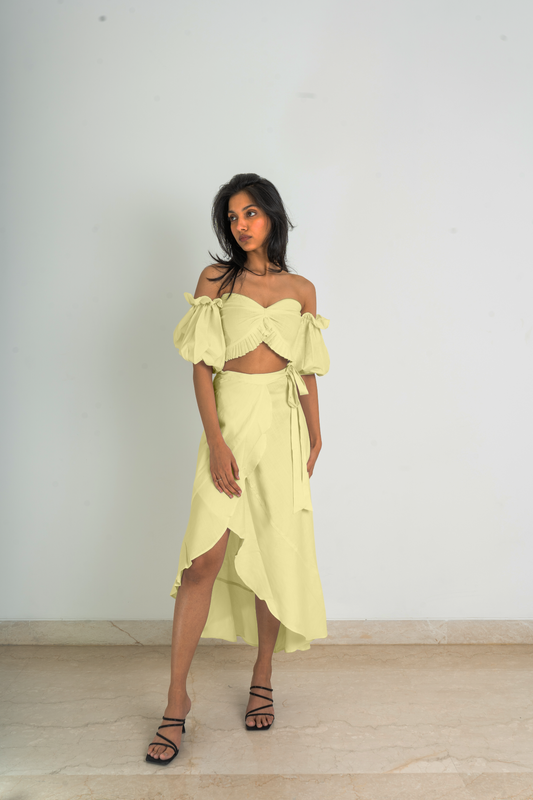 Crafted with fine linen fabric and featuring one a kind of asymmetrical cut design, this set has a strapless pleat detailed crop top with puff sleeves and a wrap-around skirt in a beautiful yellow hue.